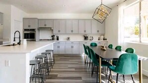 Une cuisine moderne avec des meubles blancs, un îlot central et un coin repas agrémenté de chaises vertes.