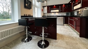 A modern kitchen with a central island, bar stools, a built-in microwave, and a dishwasher. - 2 Shanklin Manor (Shanklin)