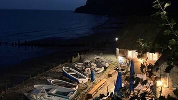 A beachside property with several boats docked, a thatched-roof building, and a view of the sea.