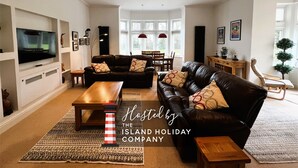 A modern living room with a large flat-screen TV, leather sofas, wooden coffee table, and a dining area with a wooden table and chairs. - 2 Shanklin Manor (Shanklin)