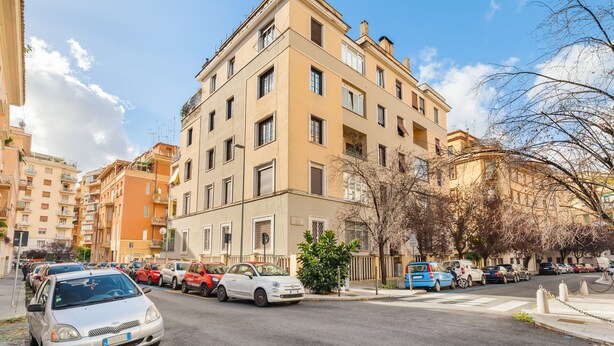 A multi-story building with a beige facade, parked cars along the street, and a clear sky. - Adelante Rooms (Rome)