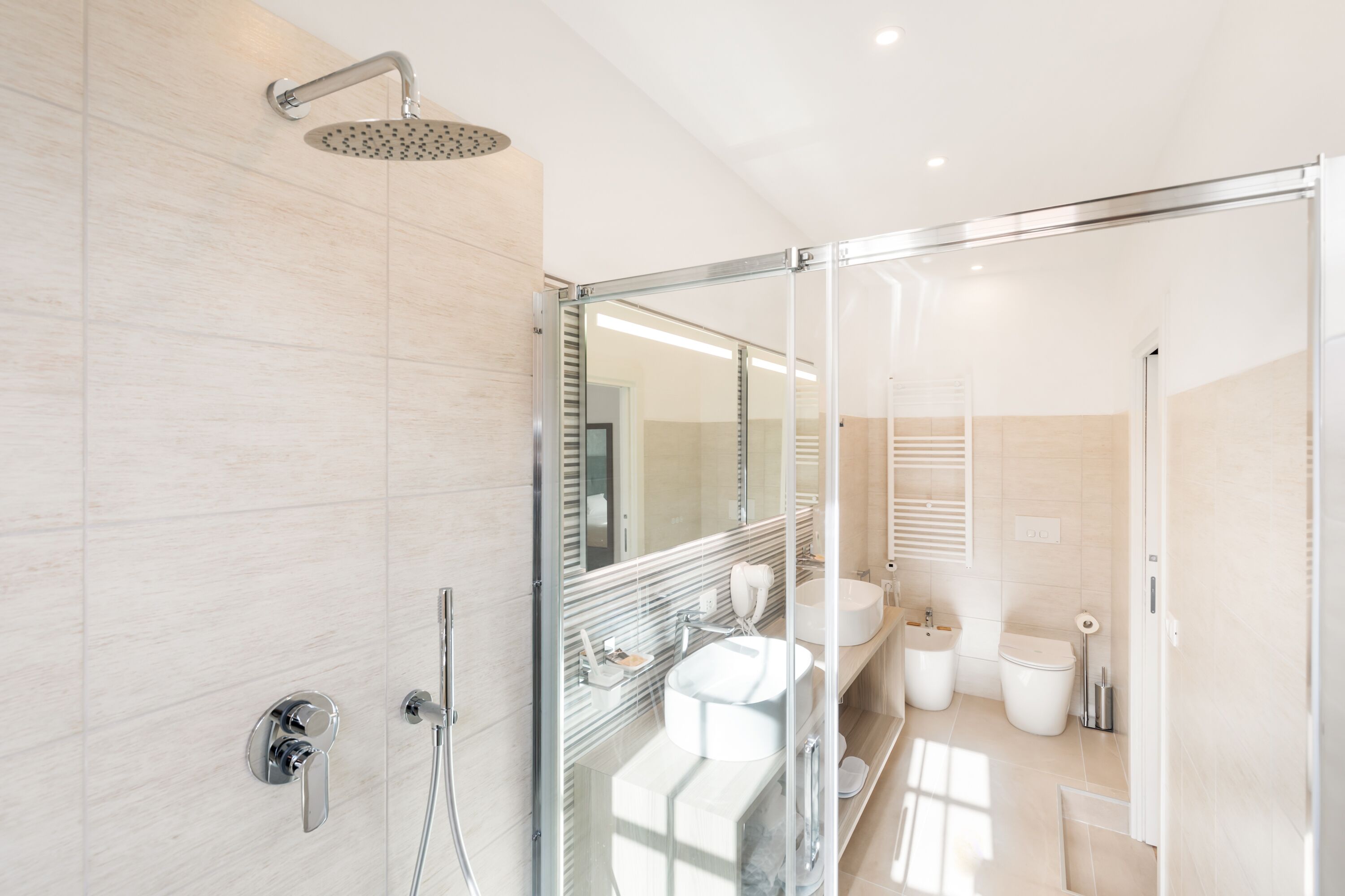 Un baño moderno con cabina de ducha de vidrio, un espejo grande y un tocador con lavabo y espejo.