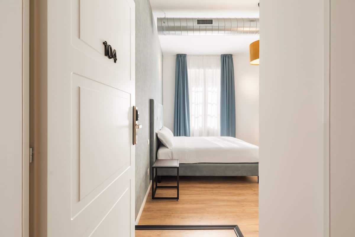A modern hotel room with a bed, a bedside table, and a window with curtains.