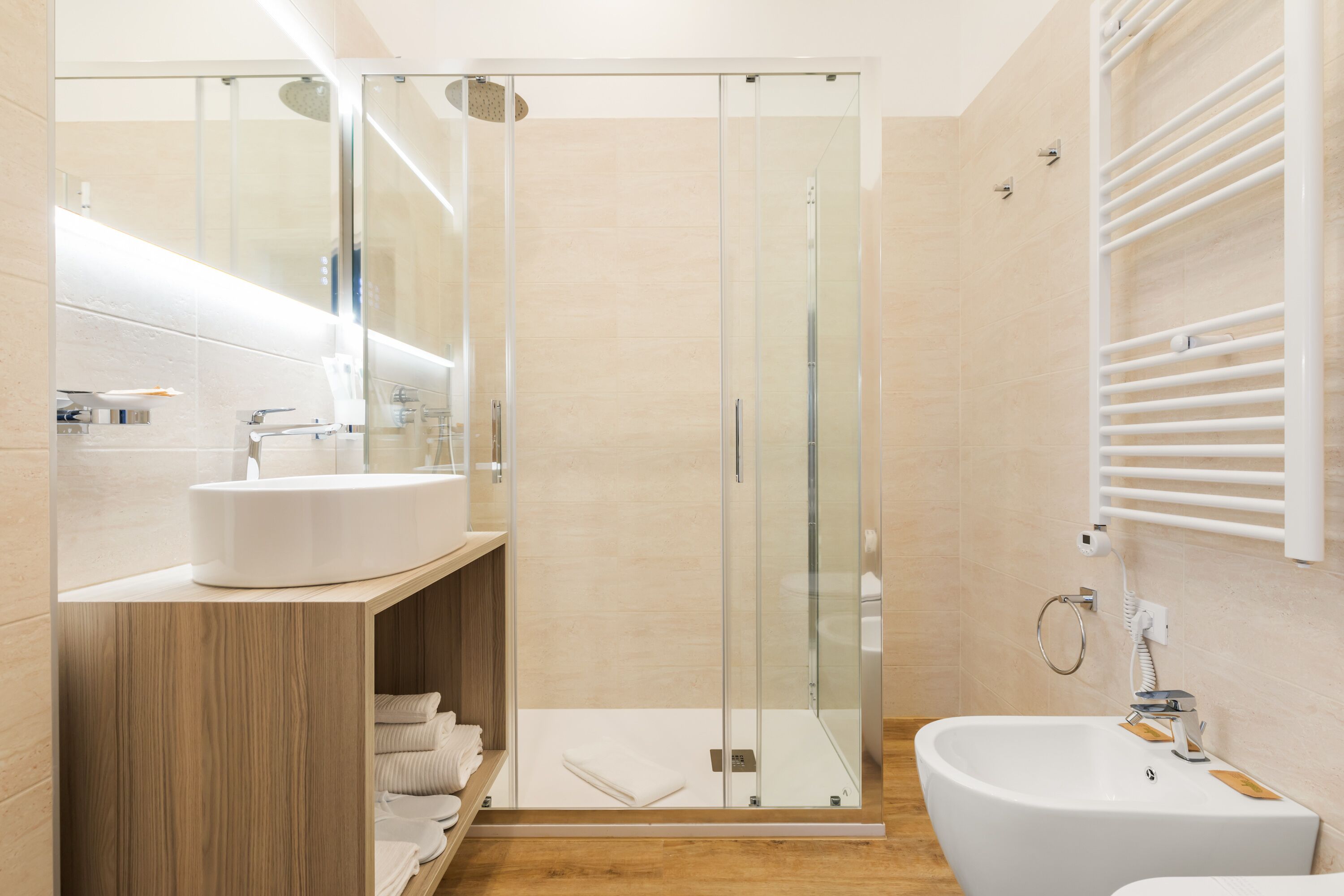 A modern bathroom with a glass-enclosed shower, a wooden vanity, and a freestanding bathtub.