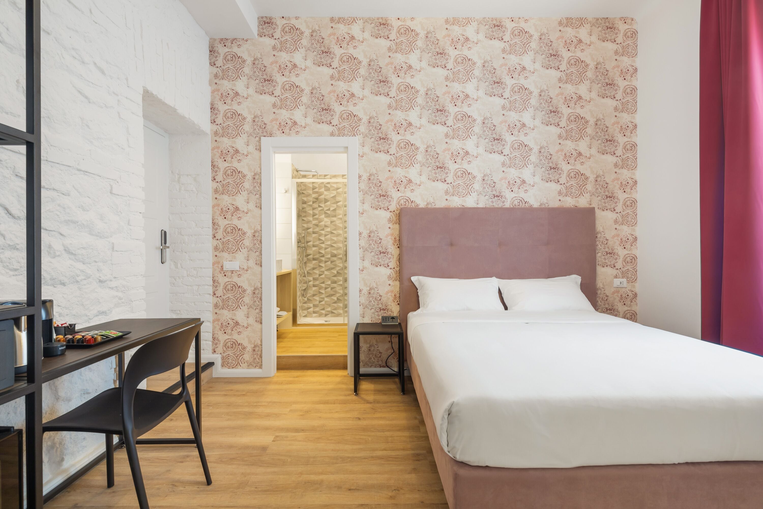 A bedroom with a bed, a desk, and a chair. There is a door leading to a bathroom.