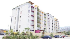 Un edificio residencial de varios pisos con balcones, un estacionamiento y vistas del paisaje circundante.
