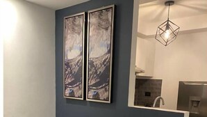 Un salón moderno con una pared de acento azul oscuro, un sofá negro con cojines blancos y dos cuadros abstractos enmarcados.