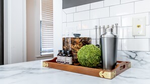 A kitchen counter with a marble surface, a wooden tray with a green spherical object, a stainless steel bottle, and two small bottles with labels.