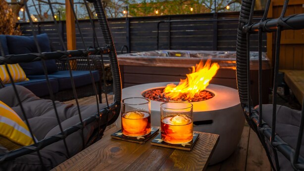 A cozy outdoor seating area with a fire pit, two glasses of a beverage, and a wooden table.