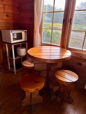 A wooden interior with a round table and stools, a microwave, and a shelf unit.