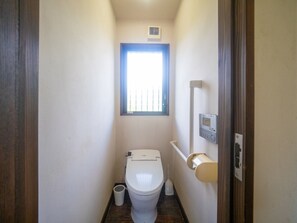 Ein schmales Badezimmer mit Toilette, Fenster und einem Händetrockner.