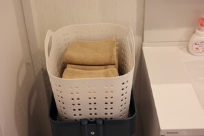 Ein Wäschekorb mit gefalteten Handtüchern in einem Raum mit weißer Wand und einem weißen Gerät.