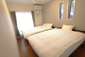 Ein Hotelzimmer mit zwei Einzelbetten, einem Fenster mit Vorhängen, einer Klimaanlage und einem gerahmten Bild an der Wand.