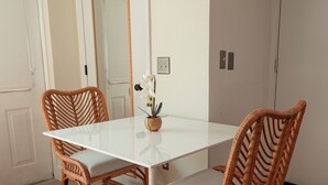 A dining area with a white table, wicker chairs, a small plant, and a mirror on the wall. - Seahorse Beach Bungalows (Fort Pierce)