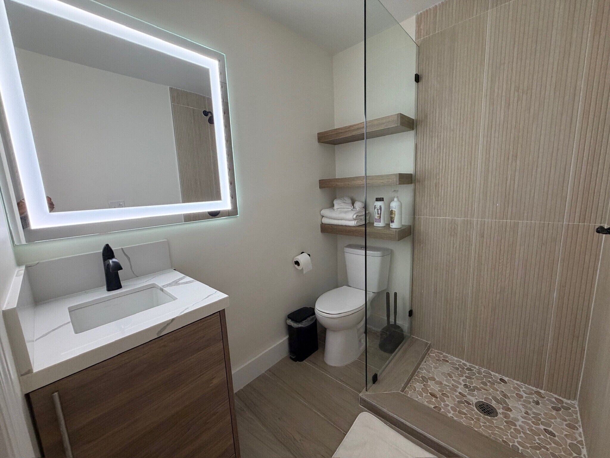 Un baño moderno con cabina de ducha de vidrio, tocador con espejo y estantes empotrados.