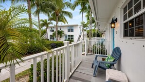 A white building with a porch, a blue chair, and a white railing. - Seahorse Beach Bungalows (Fort Pierce)