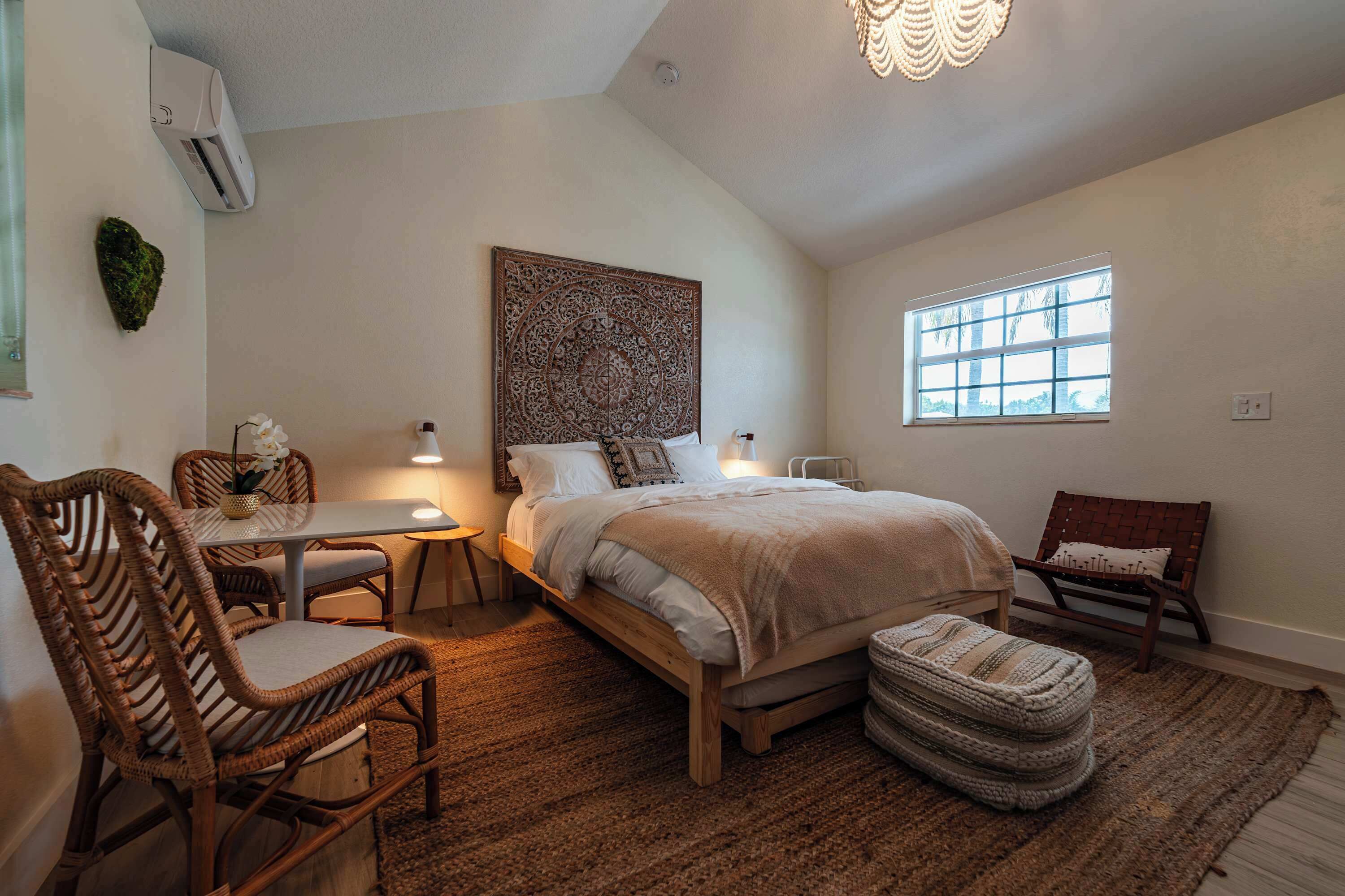 Ein Schlafzimmer mit einem Bett, zwei Stühlen, einem kleinen Tisch, einem Fenster und einer Klimaanlage.