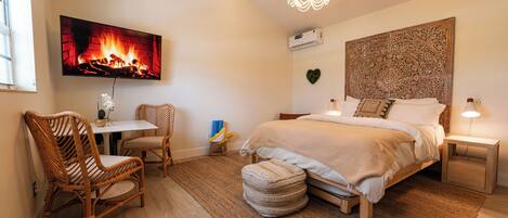 A bedroom with a bed, a chair, a table, a wall-mounted TV, and a decorative wall piece.