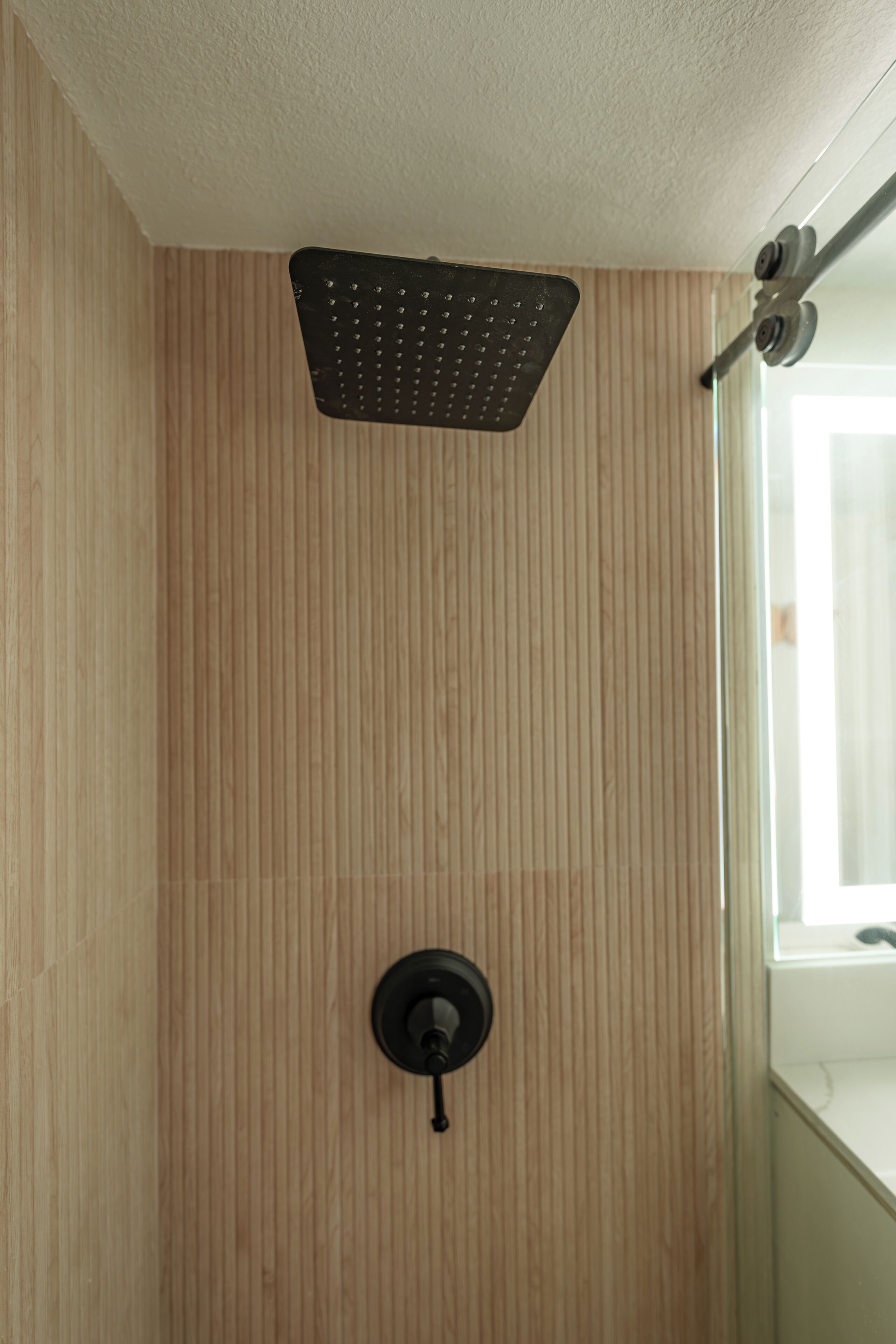 Une douche dotée d’un pommeau de douche à effet pluie, d’un panneau de commande mural et d’une porte en verre.