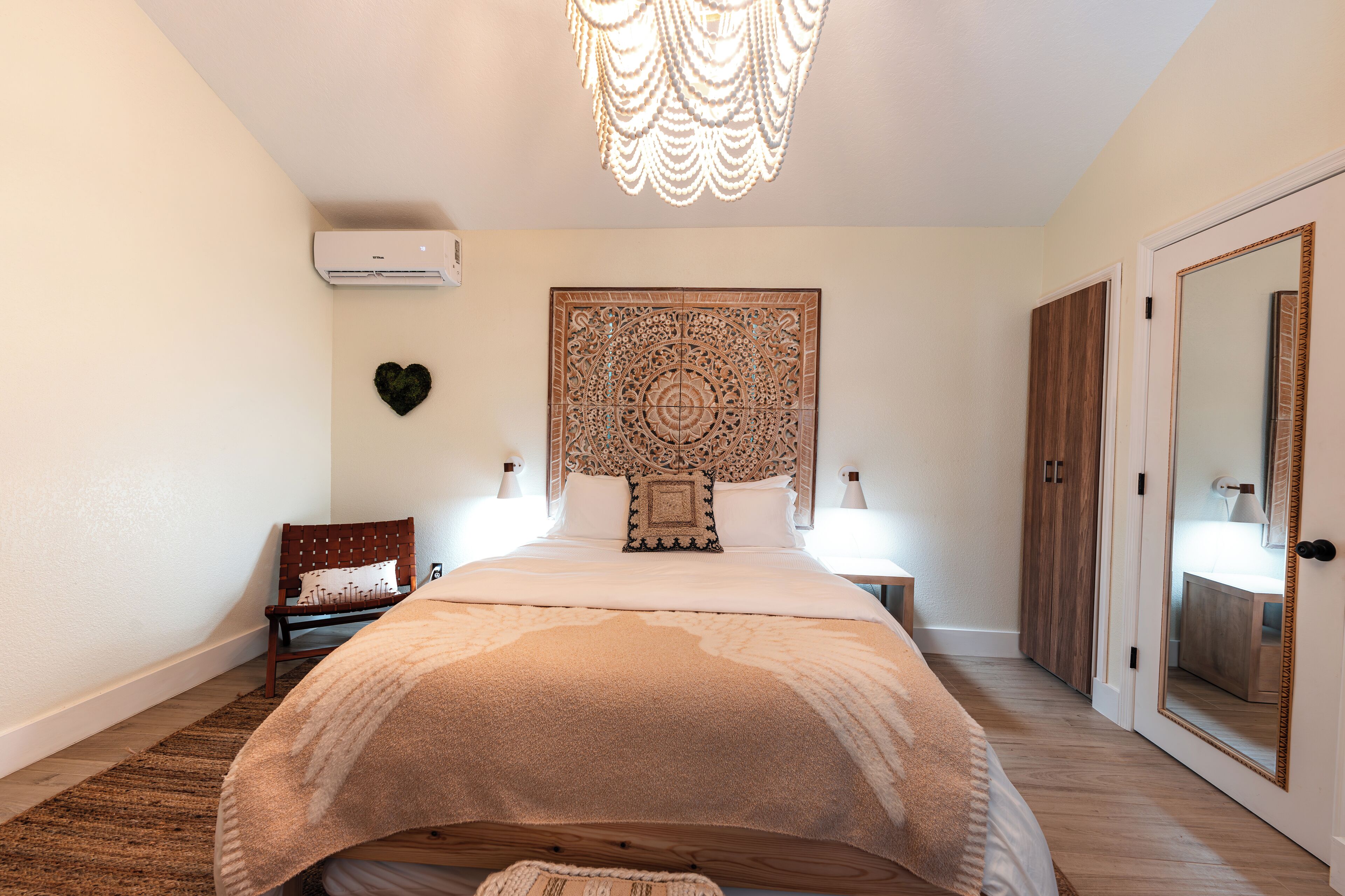 A bedroom with a large bed, a decorative headboard, a wall-mounted air conditioner, a chair, and a wardrobe.
