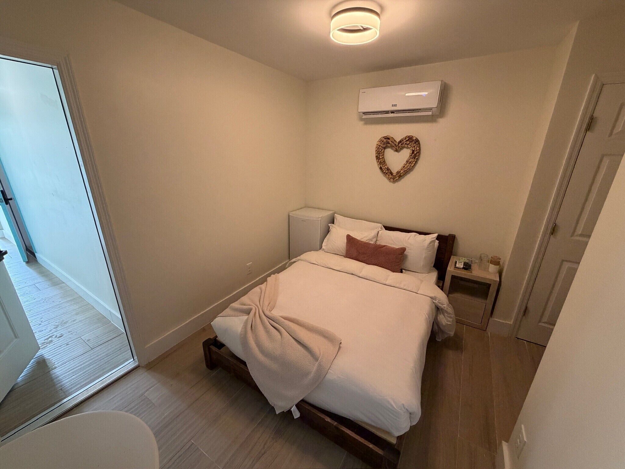 A bedroom with a bed, bedside tables, an air conditioner, a heart-shaped decoration, and a door.