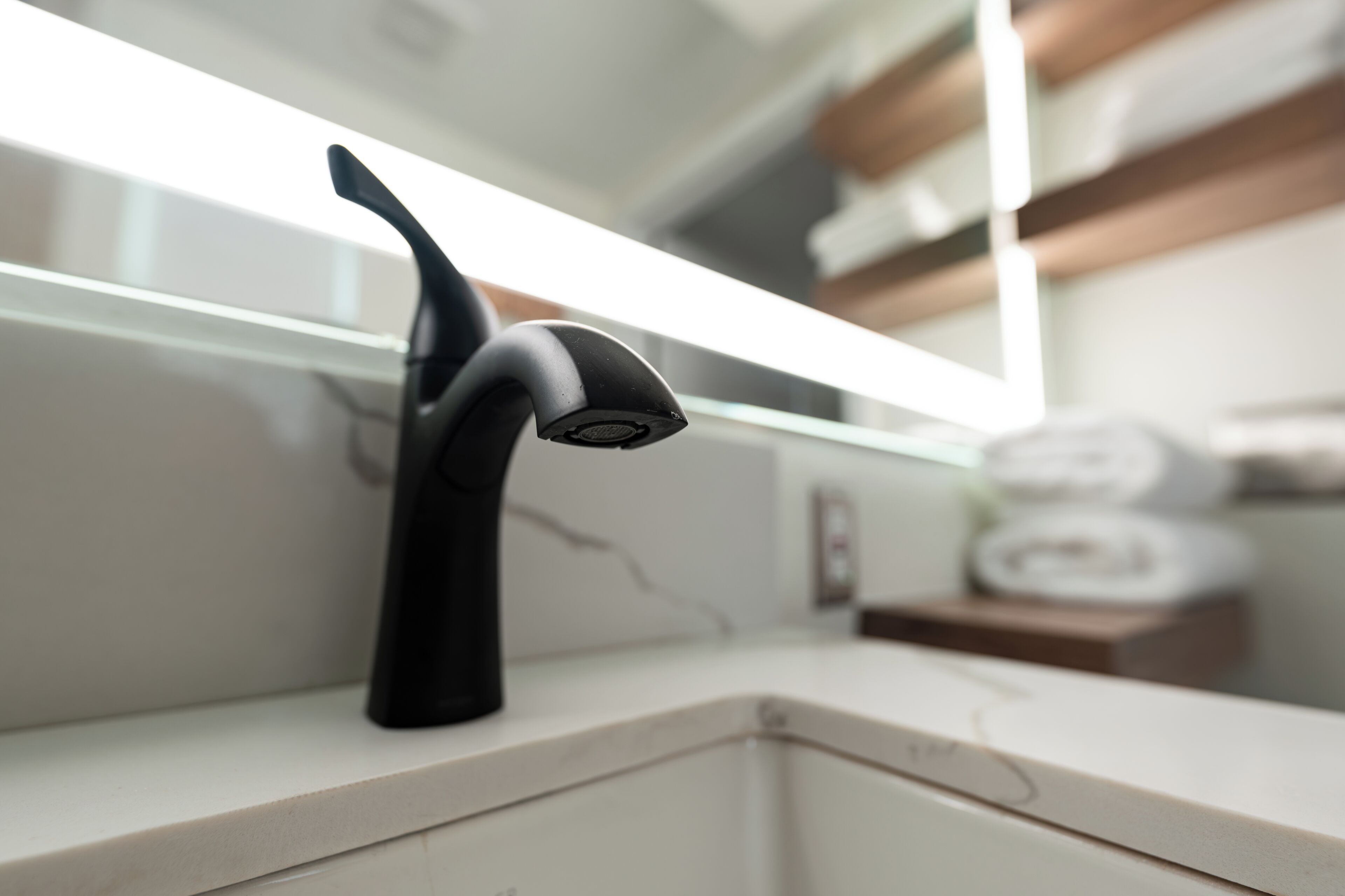 A modern bathroom with a sleek black faucet, a white countertop, and a towel rack in the background.