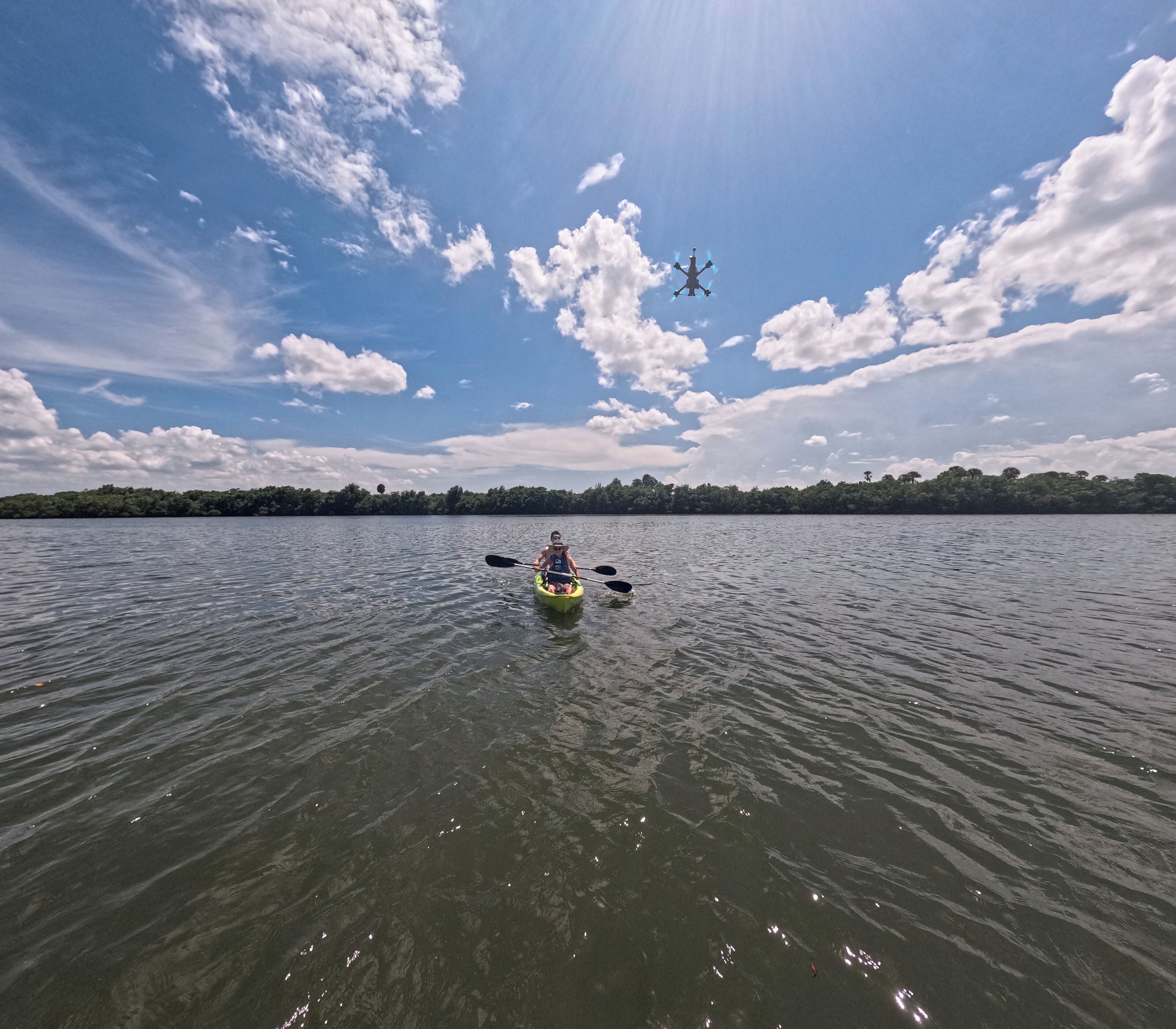 Un kayakista pagaia su un lago calmo, con cielo sereno e un drone che vola sopra.