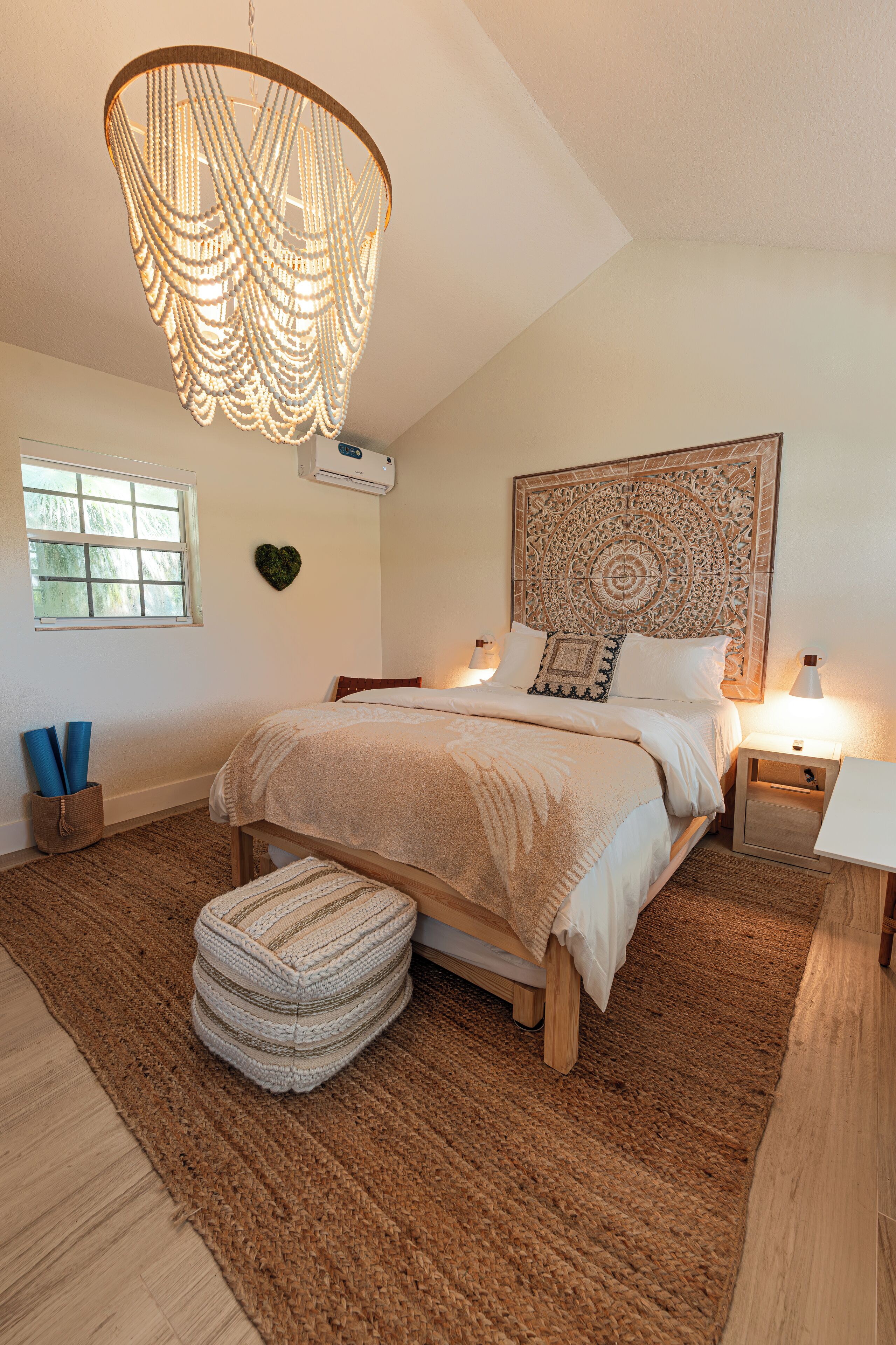 Une chambre dotée d’un grand lit, d’un tapis tissé, d’un banc en bois, d’un climatiseur fixé au mur et d’un luminaire décoratif au plafond.