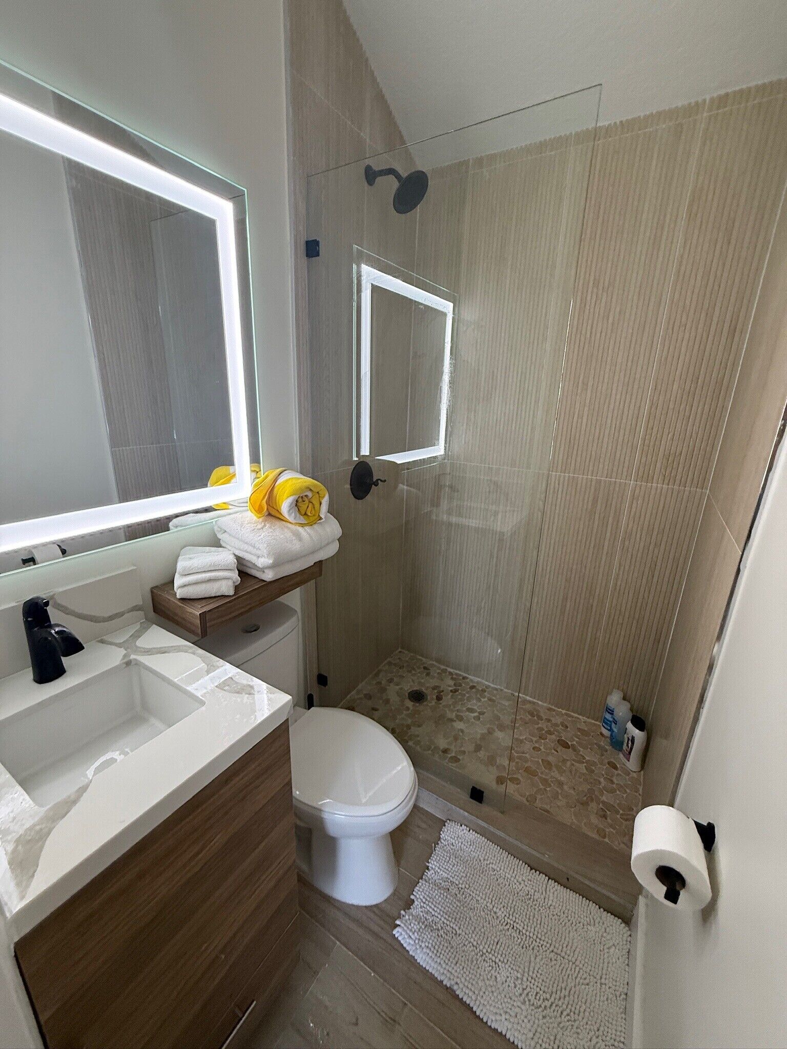 Un baño con ducha, inodoro, lavamanos y espejo.