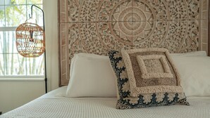 A bed with a patterned throw pillow, a hanging light fixture, and a decorative wall panel. - Seahorse Beach Bungalows (Fort Pierce)