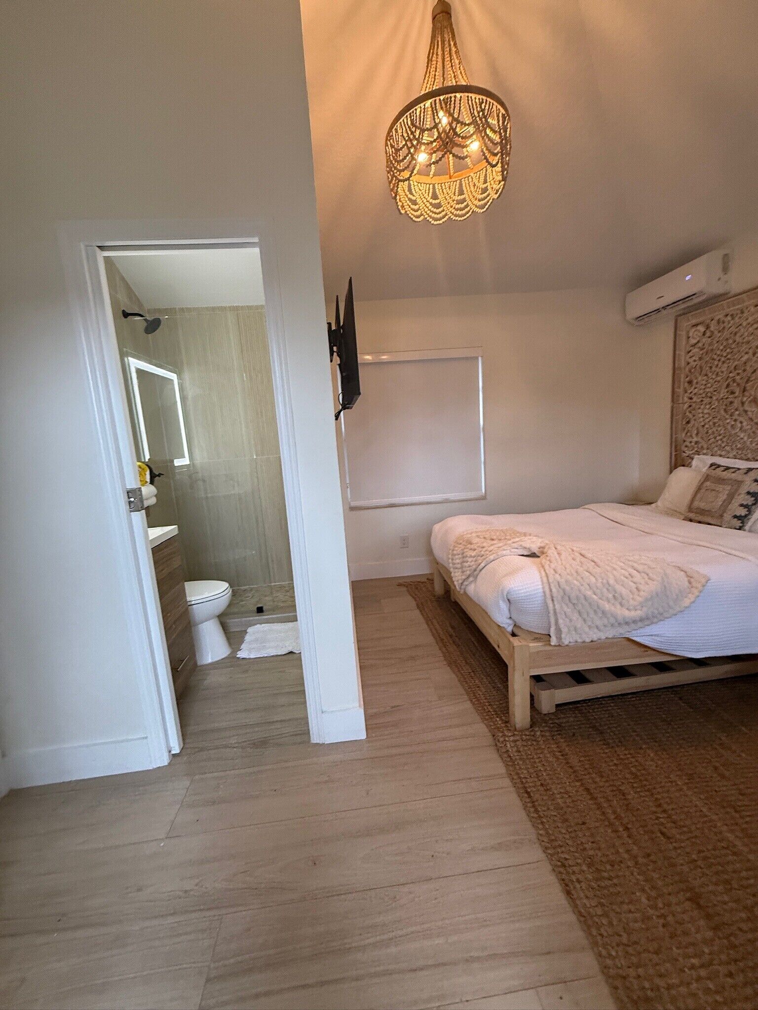 A bedroom with a bed, a wall-mounted TV, and a ceiling light fixture.