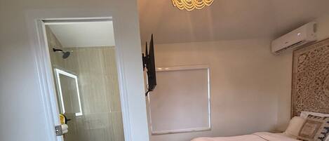 A bedroom with a bed, a wall-mounted TV, and a ceiling light fixture.