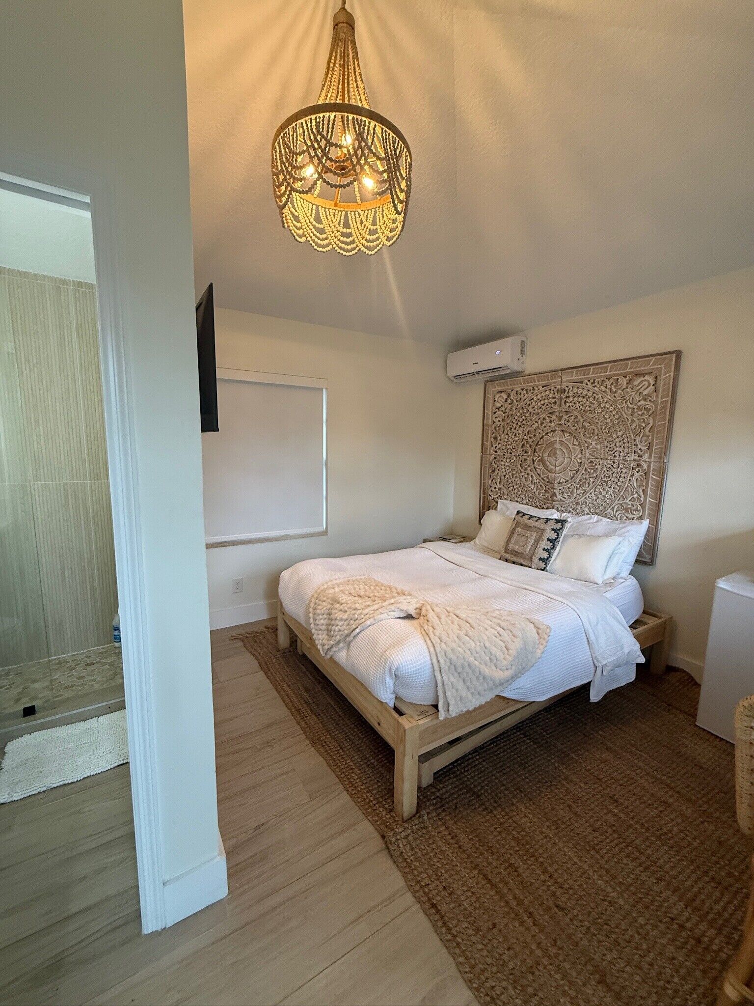 Un dormitorio con una cama de madera, un cabecero decorativo, una lámpara colgante y una pared blanca.