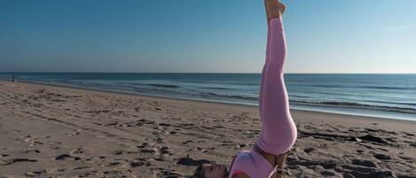 A person performing a yoga pose on a beach with a clear sky and ocean in the background.