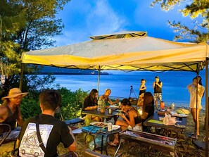 Un gruppo di persone cena all'aperto sotto una tettoia con vista sul mare.