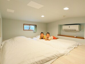 Una camera da letto con un letto grande, una finestra con tende, un condizionatore d'aria e una mensola in legno.