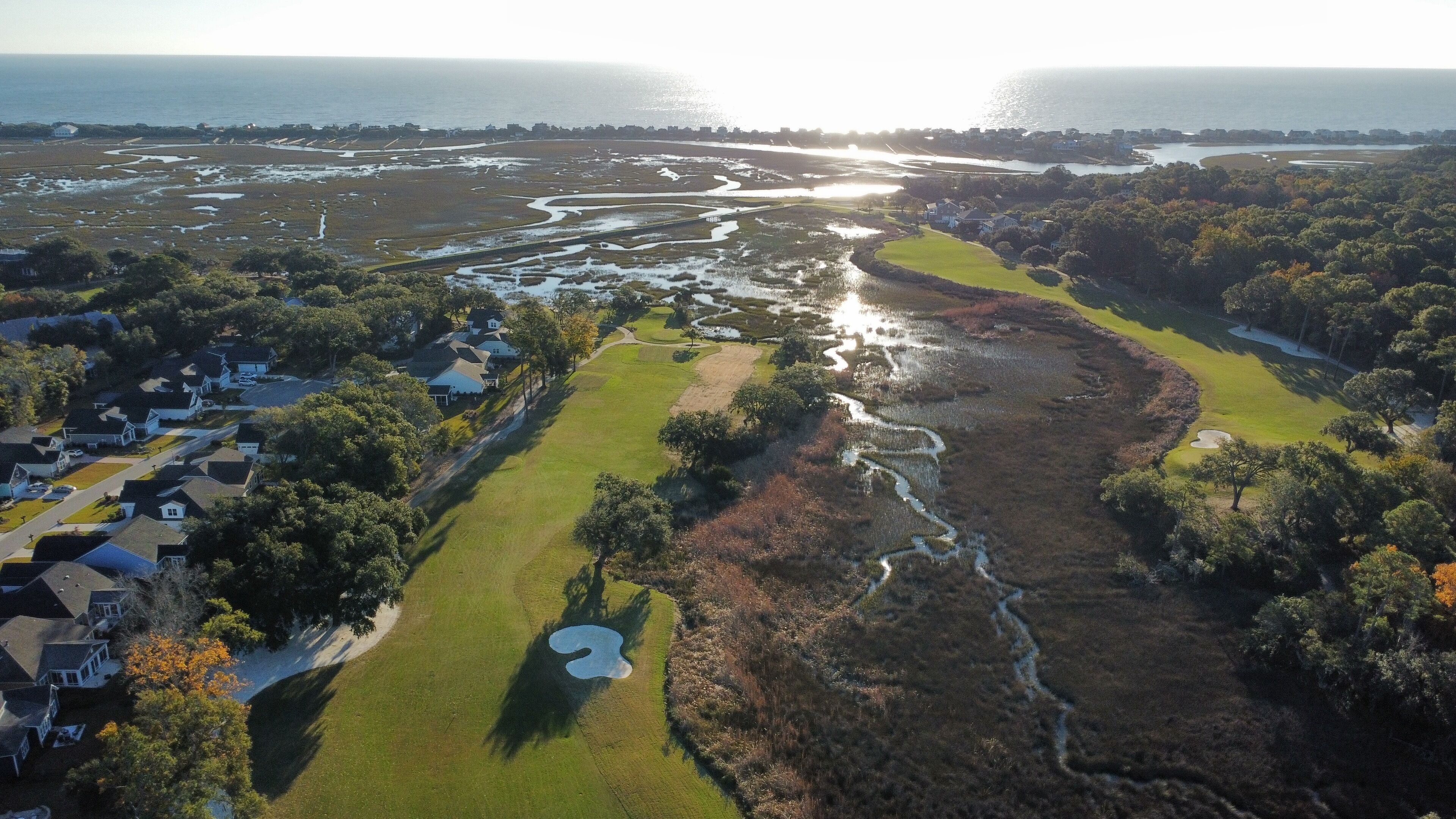 Ett flygbildsbild av ett kustområde med en golfbana, bostadshus och en vattenyta.