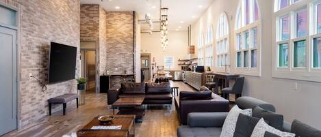 A spacious living area with a brick wall, wooden flooring, and large windows.