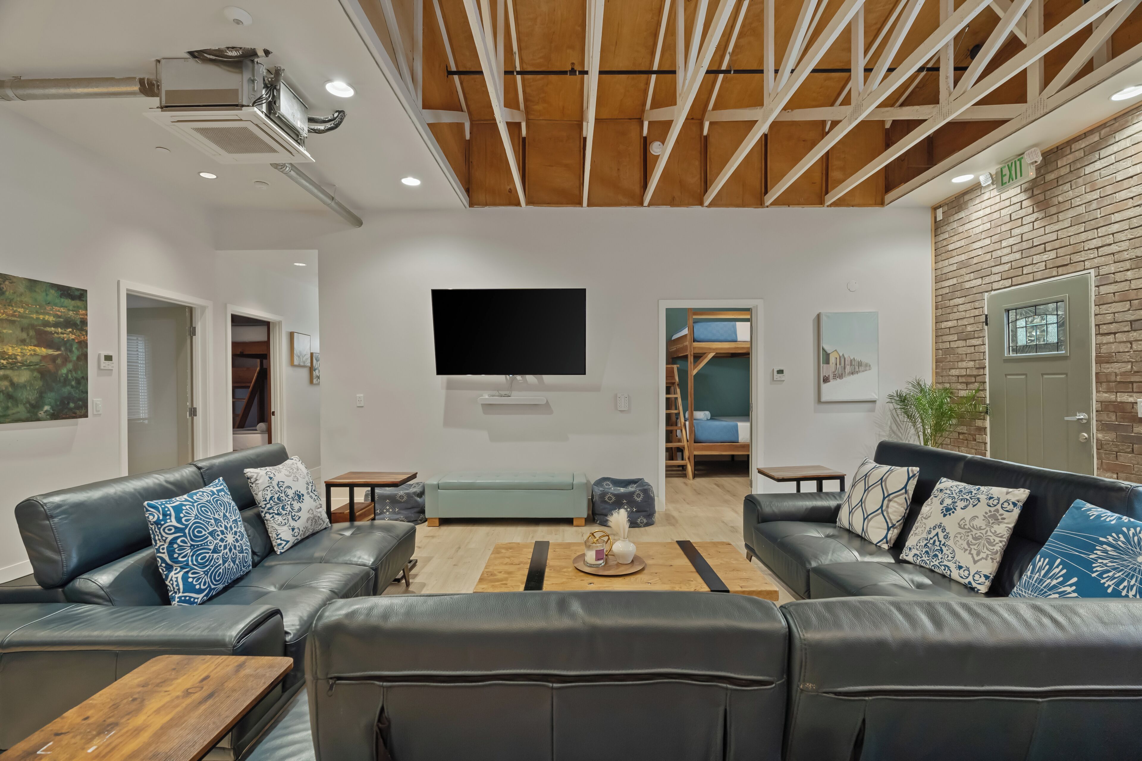 A modern lounge area with leather sofas, a flat-screen TV, and a wooden ceiling.