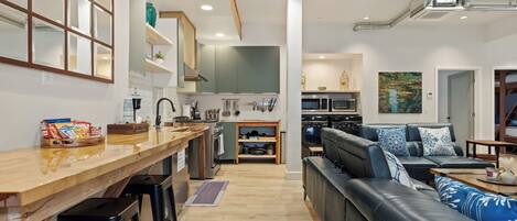 A modern kitchen with wooden countertops, a built-in oven, and a dining area with a long table and bar stools.