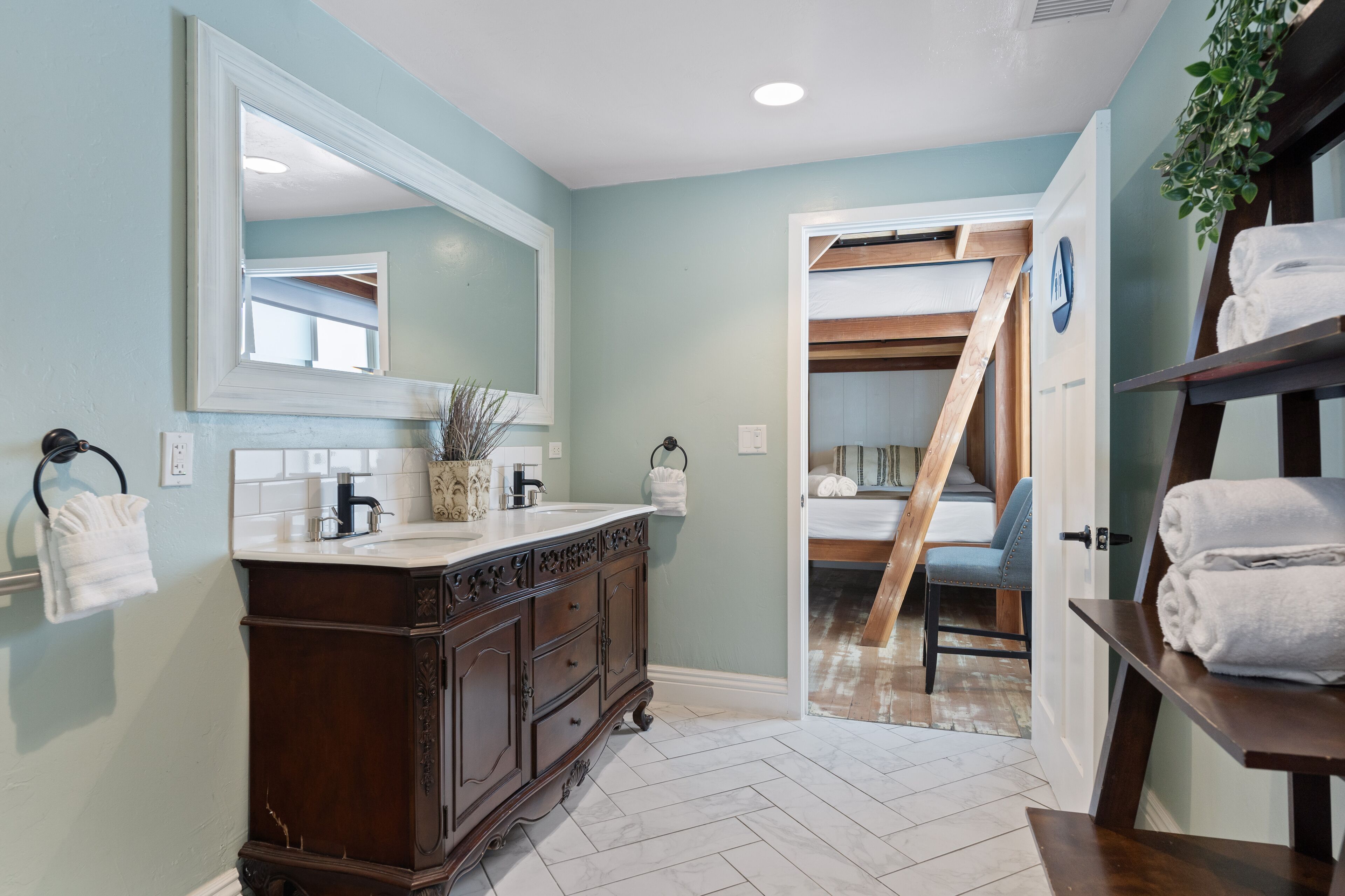 Une salle de bain avec un meuble-lavabo en bois, un grand miroir et un sol à motifs en chevrons.