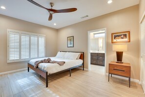 Ein Schlafzimmer mit Bett, Deckenventilator, Nachttisch und angrenzendem Badezimmer.