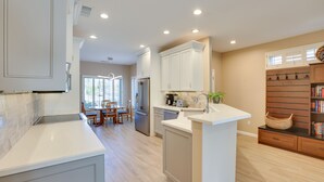 A modern kitchen with white cabinetry, a central island, and a dining area with a wooden table and chairs. - Hike & Golf! Extended Surprise Stay w/ Pool Access (Surprise)