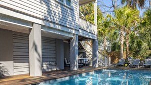 A swimming pool with a wooden deck, a white building with balconies, and palm trees in the background. - 5BR 4.5 BA Beach House close to beach on IOP with Private Pool! (Isle of Palms)