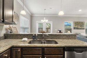 A kitchen with granite countertops, a stainless steel sink, wooden cabinets, a clock, and pendant lighting. - Waves n Games - Fun 3BR Pool home near Rosemary Beach, Game room, 30A and Beach (Rosemary Beach)