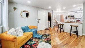 Ein modernes Wohnzimmer mit Sofa, Couchtisch, Teppich und einer Küchenzeile mit Hockern.