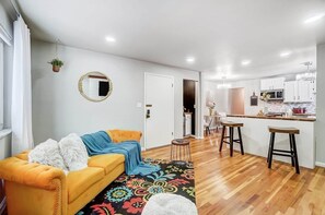 A modern living room with a sofa, a coffee table, a rug, and a kitchen area with stools. - Pleasant Ridge 2BR Furnished Apartment | Extended Stay (Cincinnati)