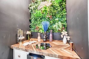 A bathroom with a wooden vanity, a mirror, a sink, a towel rack, and a wall-mounted plant arrangement. - Pleasant Ridge 2BR Furnished Apartment | Extended Stay (Cincinnati)