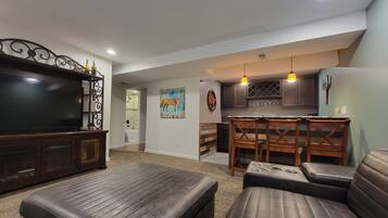 A living room with a large flat-screen TV, leather sofas, and a dining area with wooden chairs and a kitchen in the background.
