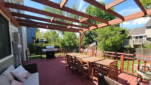 A covered deck with a wooden table and chairs, a grill, and a sofa with cushions. - Westy Escape 2 Living Rooms, 2 Primary Bedrooms, Bar, BBQ, FirePit, Patio (Westminster)
